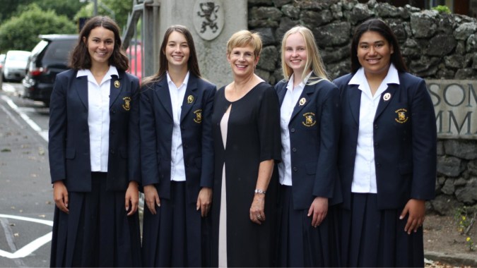 Fünf Schülerinnen in einheitlicher Schuluniform stehen vor einer Steinmauer auf dem Gelände der Epsom Girls Grammar School.