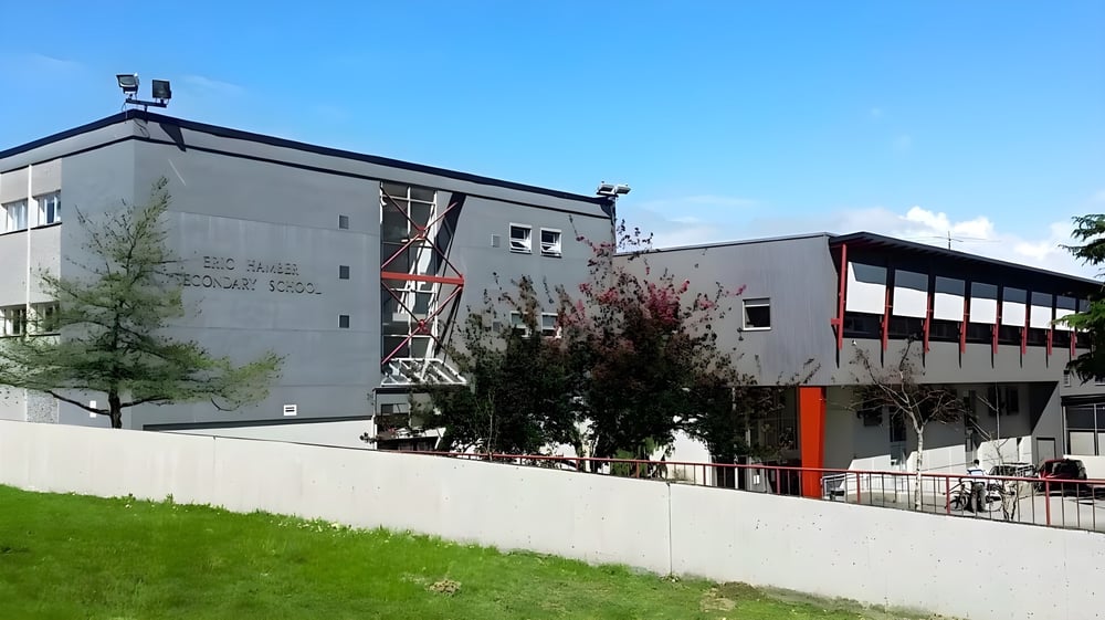 Das moderne mehrstöckige Gebäude der Eric Hamber Secondary School mit Glas- und Betonfassaden steht auf einem grasbewachsenen Gelände mit Bäumen.