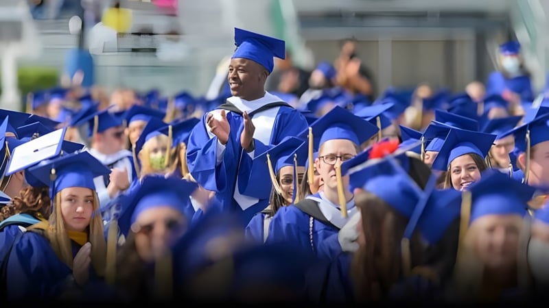 Eine große Gruppe von Absolventinnen und Absolventen in blauen Talaren steht gemeinsam vor der Erin District High School.
