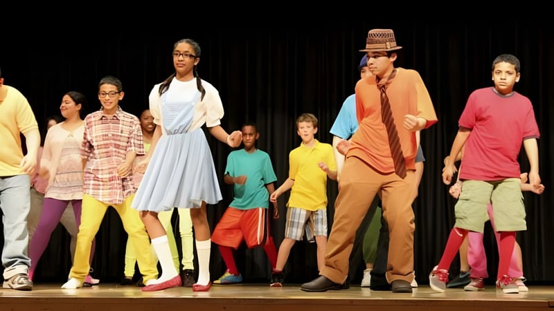 Eine Gruppe von Schülern der Erin District High School steht in bunten Outfits auf einer Bühne vor dunklem Hintergrund.
