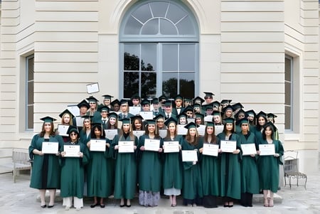 Eine große Gruppe von Absolventen der Ermitage International School in grünen Talaren steht vor einem klassischen Gebäude mit Bogenfenstern.