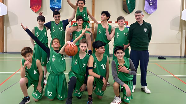 Eine Gruppe junger Basketballspielerinnen und -spieler in grünen Trikots posiert in der Sporthalle der Ermitage International School.