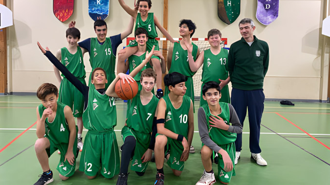 Eine Gruppe von jungen Basketballspielern in grünen Trikots spielt auf dem Sportgelände der Ermitage International School.