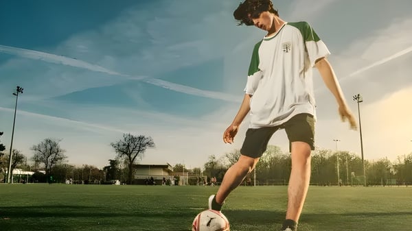 Ein Schüler der Ermitage International School steht mit einem Fußball auf dem Rasenfeld vor blauem Himmel und Bäumen.