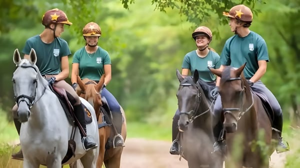 Schüler der Ermitage International School reiten in grüner Schuluniform auf einem Weg durch grünes Terrain.