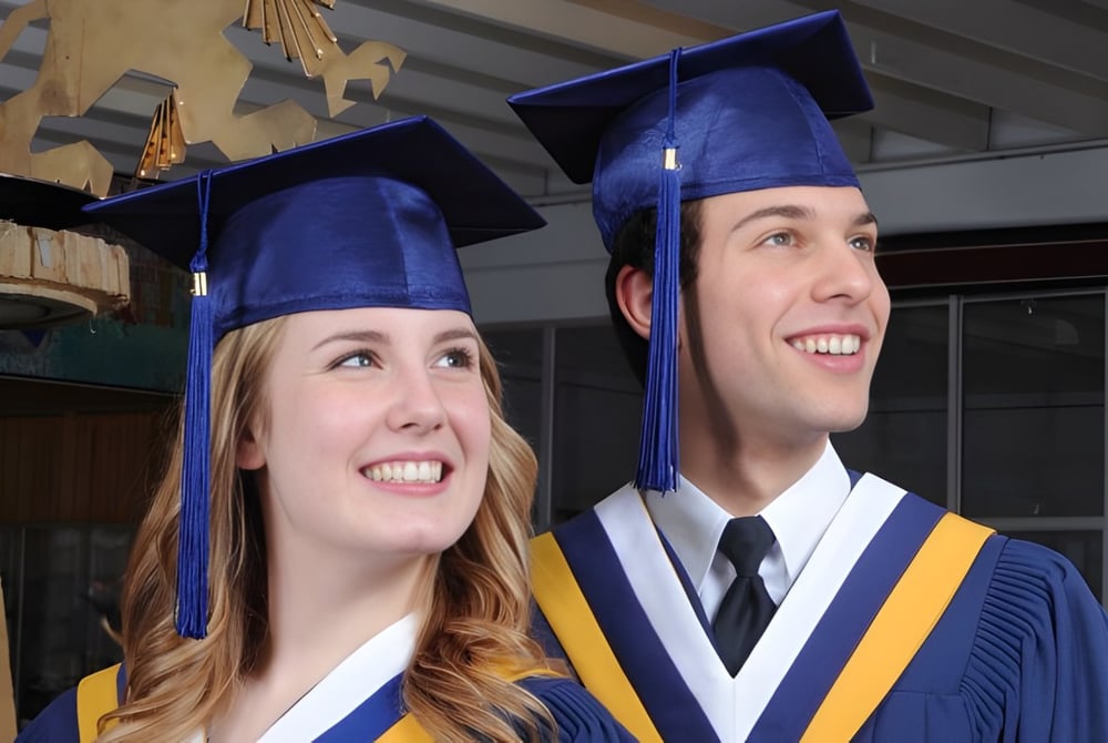 Zwei Absolventen der Ernest Manning High School in blauen Talaren stehen in einem Raum mit Holzregalen und Abschlussutensilien.