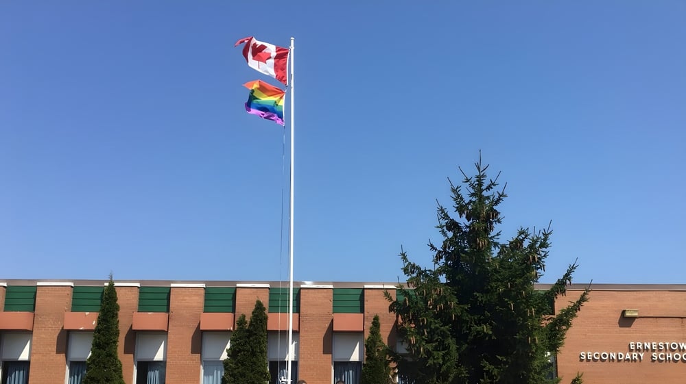 Vor dem Backsteingebäude der Ernestown Secondary School wehen eine kanadische Flagge und eine Regenbogenflagge am Fahnenmast.