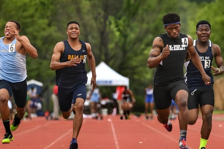 Eine Gruppe von Schülerinnen und Schülern der Ernestown Secondary School läuft auf der Laufbahn mit einem Sportfeld und Bäumen im Hintergrund.