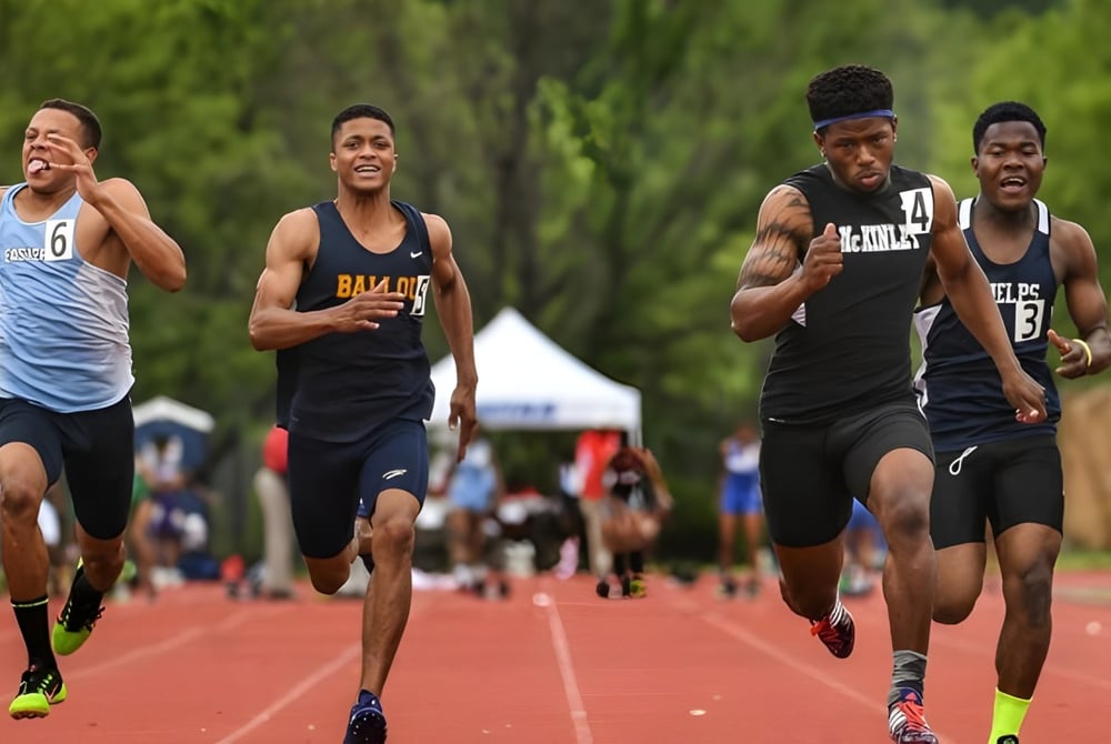 Eine Gruppe von Schülerinnen und Schülern der Ernestown Secondary School läuft auf der Laufbahn mit einem Sportfeld und Bäumen im Hintergrund.