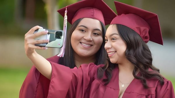 Zwei Schülerinnen in Abschlusskleidung der Escondido Charter High School machen gemeinsam ein Selfie im Freien.