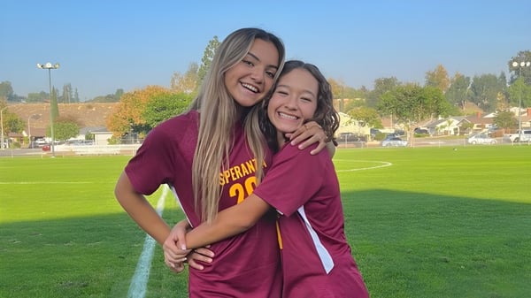 Zwei Schülerinnen in roten Trikots umarmen sich auf einem Feld auf dem Campus der Esperanza High School.