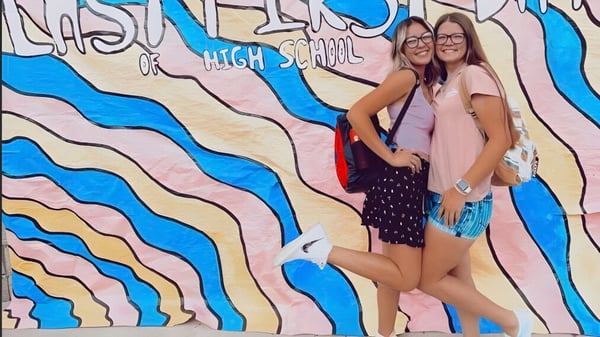 Zwei Schülerinnen posieren vor einem farbenfrohen Wandbild mit dem Schriftzug High School an der Esperanza High School.