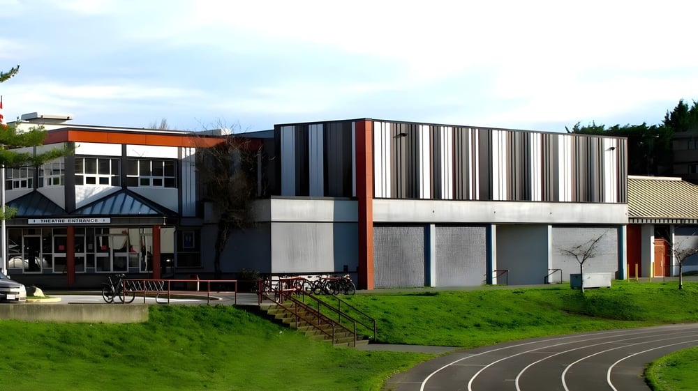 Das moderne mehrstöckige Gebäude der Esquimalt High School steht vor einer Rasenfläche und einem geschwungenen Weg.