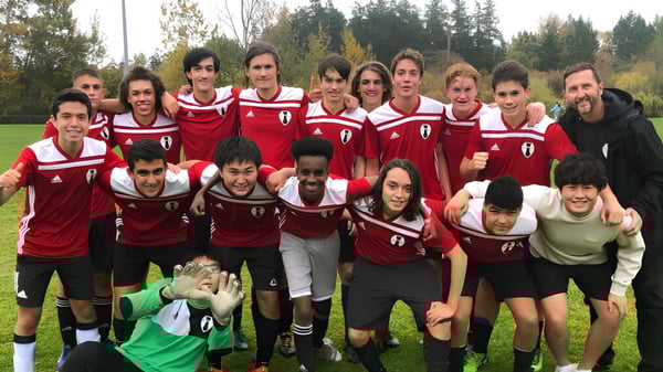 Eine Gruppe von Schülern der Esquimalt High School posiert gemeinsam auf einem Spielfeld mit Bäumen im Hintergrund.