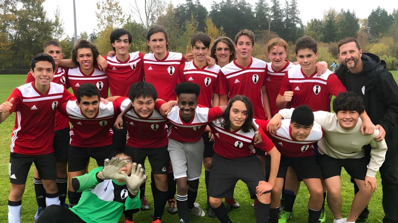 Eine Gruppe von Schülern der Esquimalt High School posiert gemeinsam auf einem Spielfeld mit Bäumen im Hintergrund.