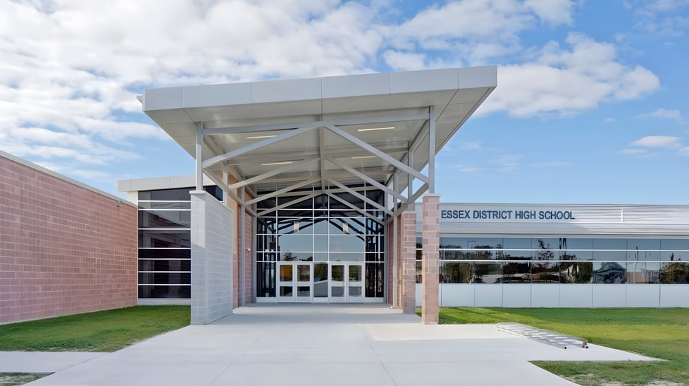 Das moderne Schulgebäude der Essex District High School mit Glasfassade und markanter Architektur vor blauem Himmel.