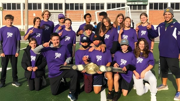 Eine Gruppe von Schülerinnen und Schülern in lila Shirts steht gemeinsam auf dem Sportfeld des Etobicoke Collegiate Institute vor einem Backsteingebäude.