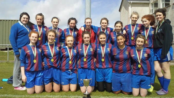 Eine Gruppe von Schülerinnen der Eureka Secondary School steht mit Medaillen auf einem Fußballfeld.