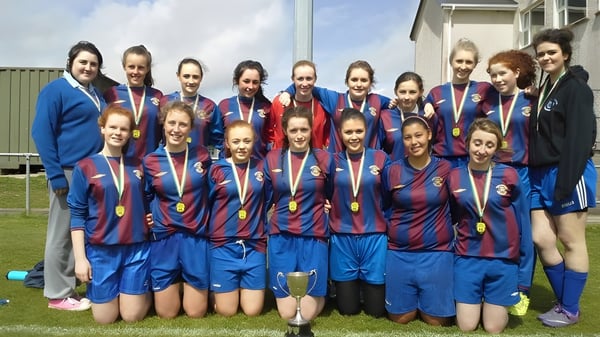 Eine Gruppe Schülerinnen der Eureka Secondary School posiert gemeinsam in blauen und roten Trikots auf einem Fußballfeld.
