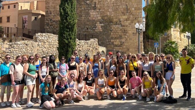 Eine große Gruppe Schülerinnen und Schüler der Eureka Secondary School versammelt sich im Freien vor historischen Steinbauten und grüner Umgebung.