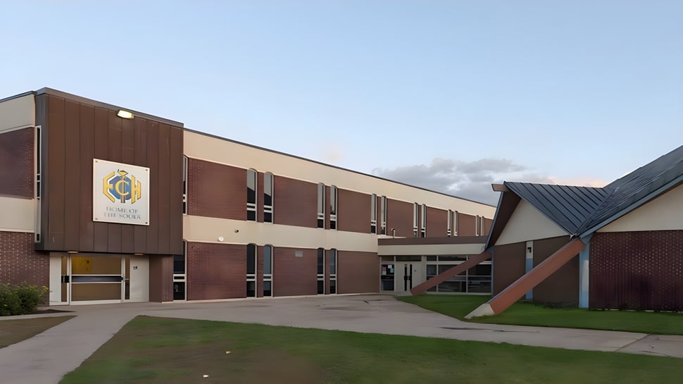Das mehrstöckige Backsteingebäude mit dem Logo der Evan Hardy Collegiate steht auf einem grünen Gelände unter blauem Himmel.