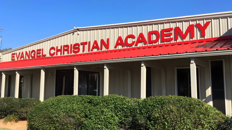 Das Hauptgebäude der Evangel Christian Academy mit rotem Dach ist von Büschen und Bäumen umgeben.