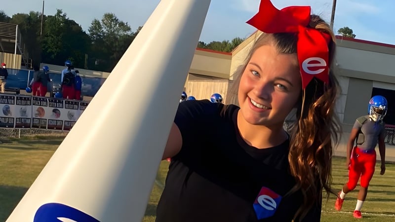 Eine junge Frau mit roter Schleife im Haar steht lächelnd vor dem Sportfeld der Evangel Christian Academy.