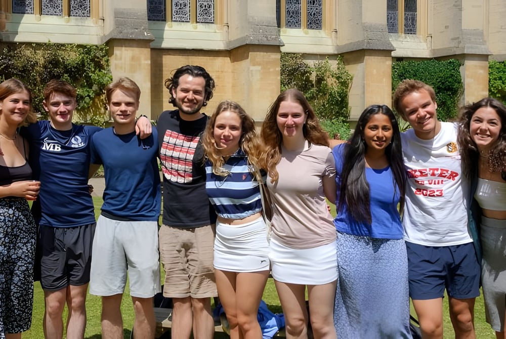 Eine Gruppe von Schülerinnen und Schülern steht vor einem Gebäude mit verzierter Architektur auf dem Campus des Exeter College.