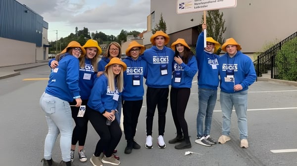 Eine Gruppe Schüler der Exploits Valley High School steht vor einer Baustelle mit blauen Hemden und Schutzhelmen.
