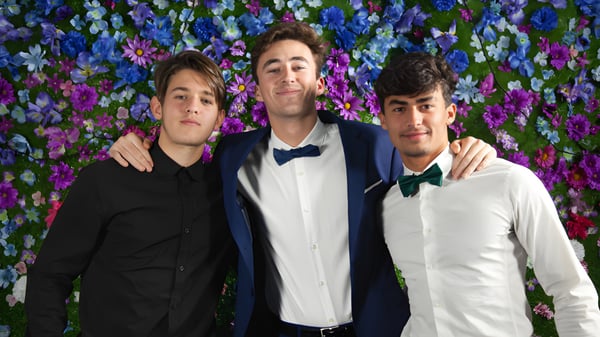 Drei Schüler des F-1 No Choice Programms USA posieren gemeinsam vor einem farbenfrohen Blumenhintergrund.