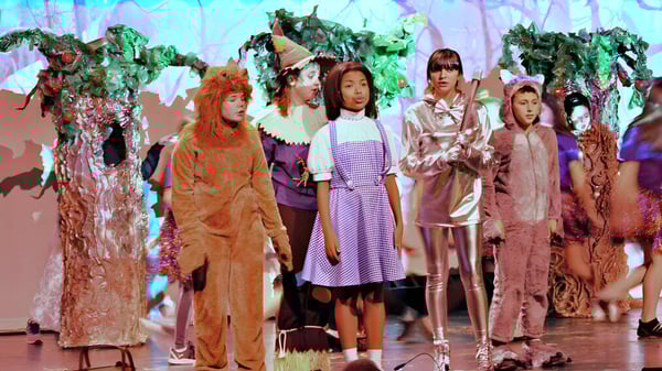 Schüler der Fabius Pompey High School tragen bunte Kostüme vor einem surrealen Hintergrund.