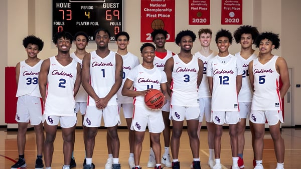 Eine Gruppe von Basketballspielern in weißen Uniformen mit dem Schriftzug Colonials in der Sporthalle der Fairfax Christian School.