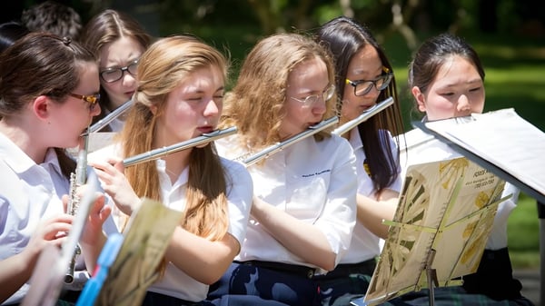 Schüler der Fairfax Christian School spielen im Freien musikalische Instrumente vor einer grünen Kulisse.