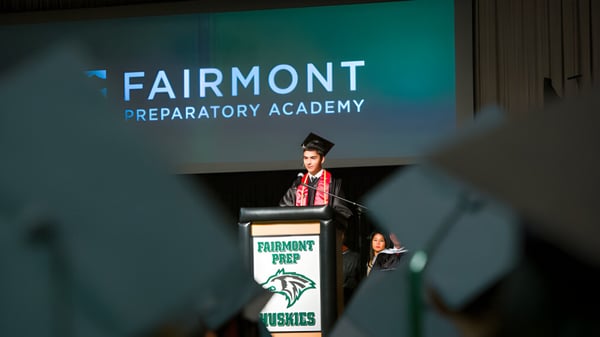 Eine Person in rotem Abschlussgewand hält eine Rede am Podium auf der Fairmont Prep Academy.