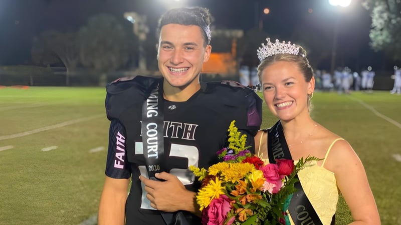 Ein Mann in einem Fußballtrikot steht neben einer Frau mit Krone und Blumen auf dem Fußballfeld der Faith Christian Academy in Florida.