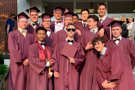 Eine Gruppe von Absolventinnen und Absolventen der Faith Christian Academy (PA) steht in roter Robe vor einem Backsteingebäude.