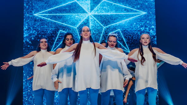Eine Gruppe von Schülerinnen der Faith Christian Academy (FL) führt auf der Bühne vor einem beleuchteten geometrischen Hintergrund eine Tanzperformance auf.
