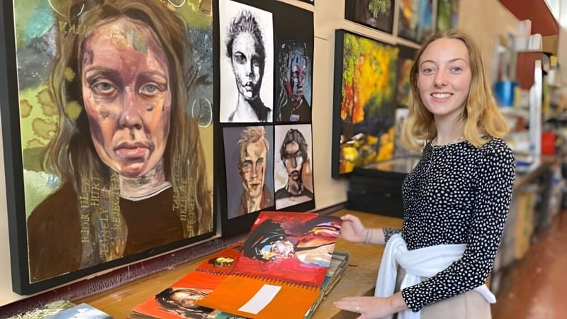 Eine Frau steht vor einer Wand mit farbenfrohen Porträts und arbeitet künstlerisch auf dem Campus der Farlington School.