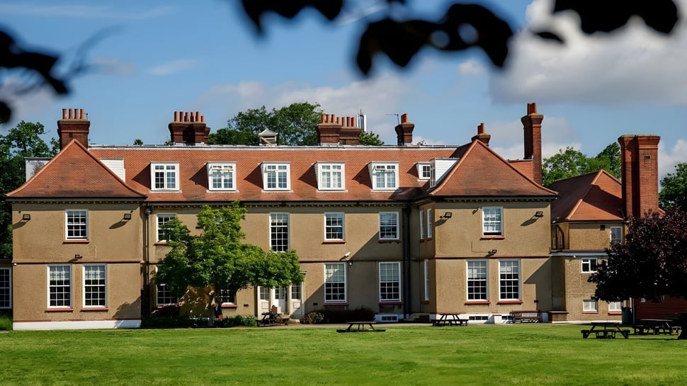 Das mehrstöckige Backsteingebäude der Farringtons School steht auf einer Wiese und ist von Bäumen umgeben.