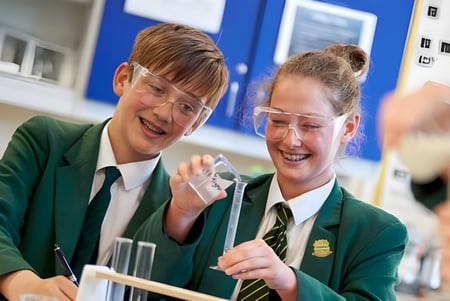 Zwei Schülerinnen der Farringtons School lachen und unterhalten sich im Klassenzimmer mit blauen Wänden.