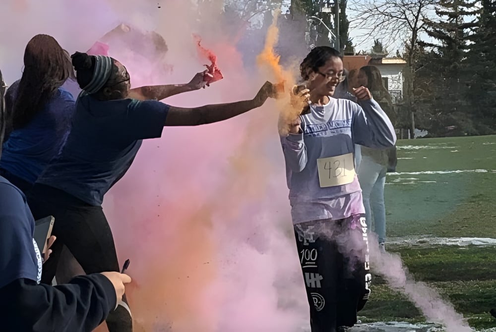 Schüler der Father Lacombe High School werfen bunte Pulver in die Luft auf einem Grasfeld.