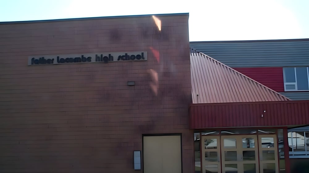 Das moderne Schulgebäude der Father Lacombe High School mit roter und brauner Fassade und dem Schulnamen an der Vorderseite.