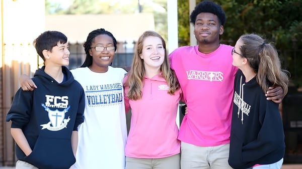 Eine Gruppe von Schülerinnen und Schülern der Fayetteville Christian School steht gemeinsam in Sporttrikots im Freien vor einem Zaun mit Bäumen.