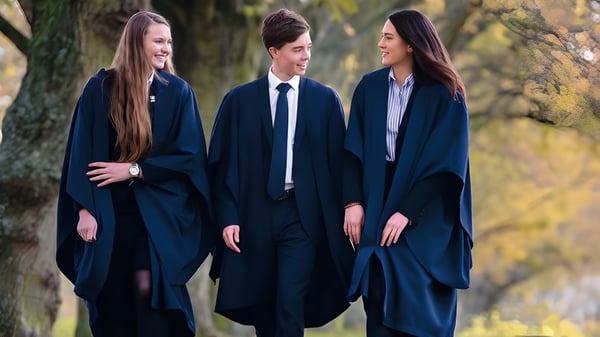 Drei Studierende der Felsted School stehen im Wald und tragen dunkle akademische Gewänder.