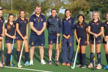 Eine Gruppe junger Hockeyspielerinnen und Hockeyspieler steht gemeinsam auf dem Sportfeld der Felsted School.