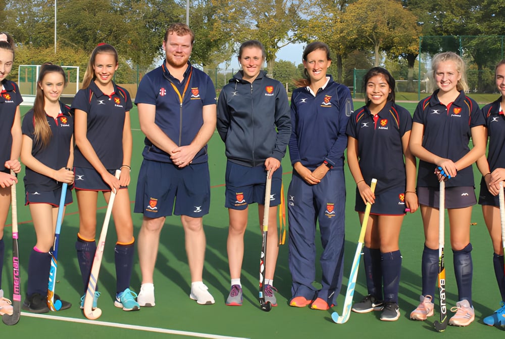 Eine Gruppe junger Hockeyspielerinnen und Hockeyspieler steht gemeinsam auf dem Sportfeld der Felsted School.