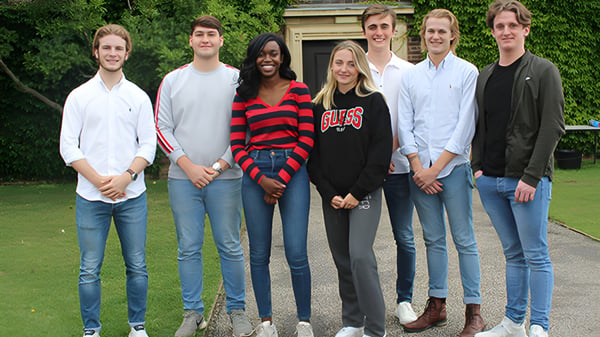 Eine Gruppe von Schülerinnen und Schülern steht auf dem Gelände der Felsted School auf einer Wiese mit Bäumen und Gebäuden im Hintergrund.