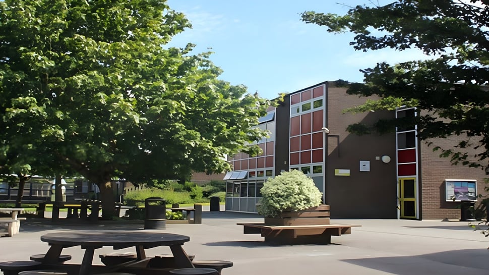 Der Innenhof der Ferndown Upper School zeigt Holzbänke vor einem Backsteingebäude und ist von Bäumen umgeben.