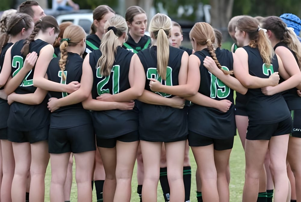 Eine Gruppe junger Sportlerinnen steht auf einem Sportfeld der Ferny Grove State High School vor Bäumen und Gebäuden.