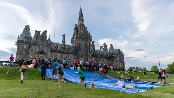Das große, kathedralenähnliche Gebäude des Fettes College steht im Hintergrund über einem Grasfeld mit einer Gruppe von Menschen.